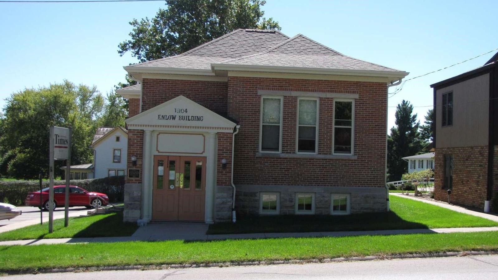 A brick, two story building has a white trimmed portico and three tall windows in front.