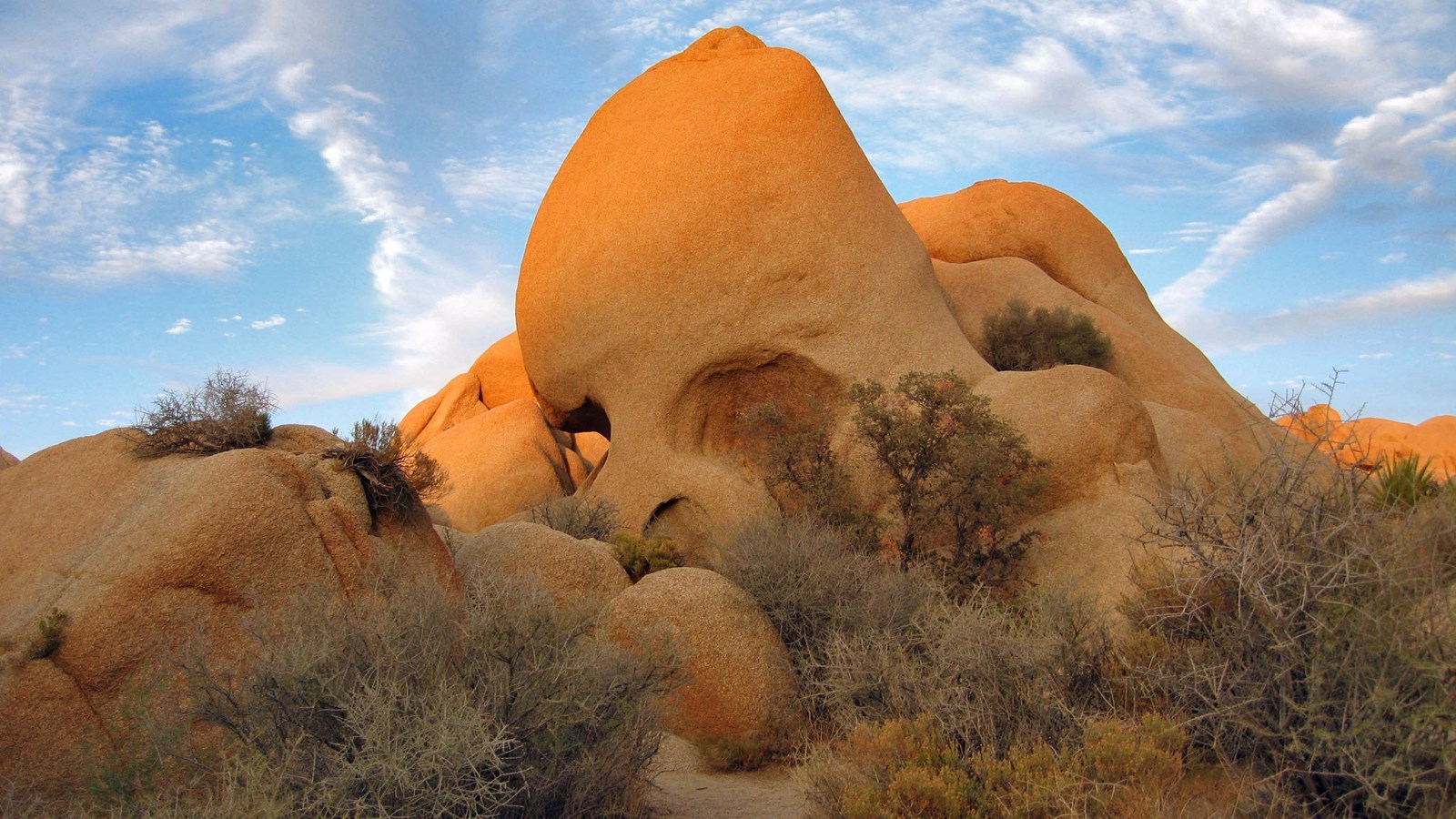 A large rock with two holes resembling eye sockets sticking out of a rock and boulder field.