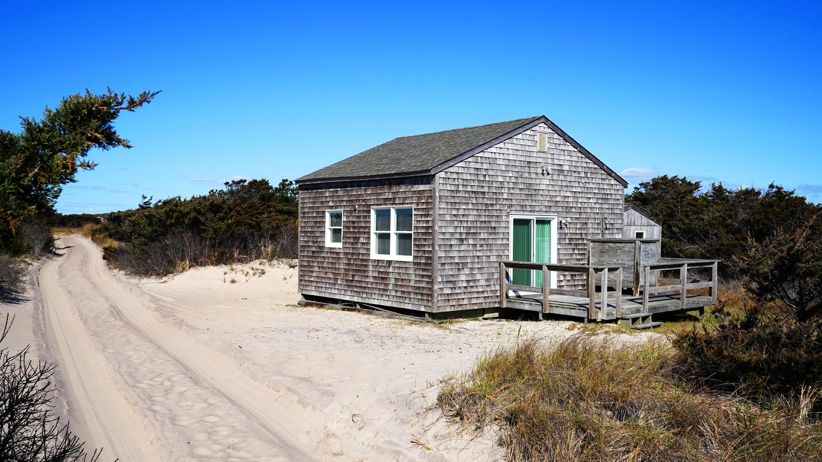 A small wooden-shingled cottage near a sandy road.