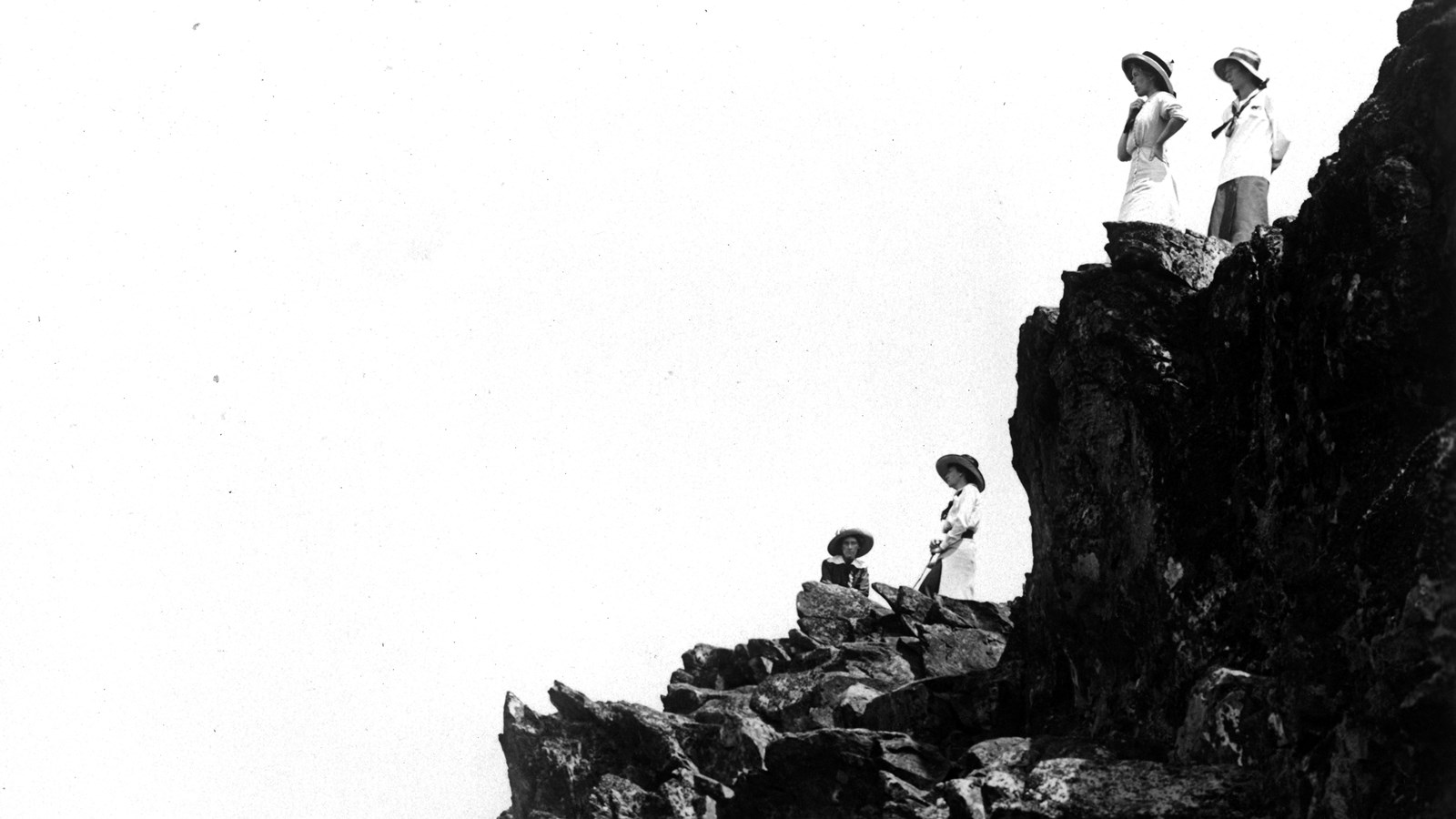 A black-and-white photo of 4 women in dresses and sunhats enjoying the view from Stony Man
