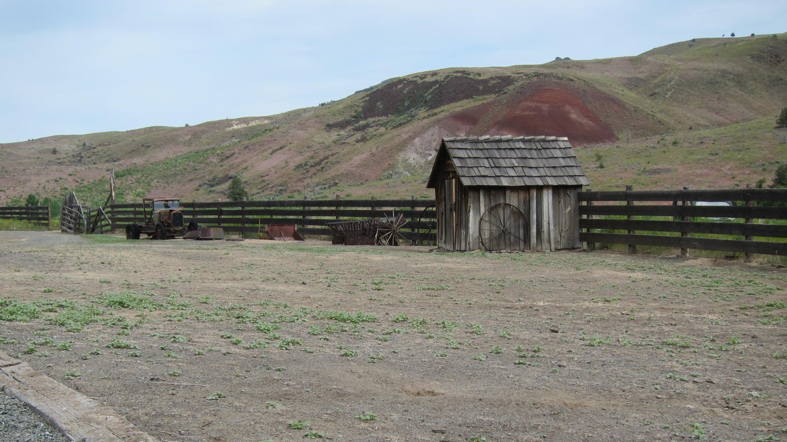 A small log shed near old farm equipment on barren ground.