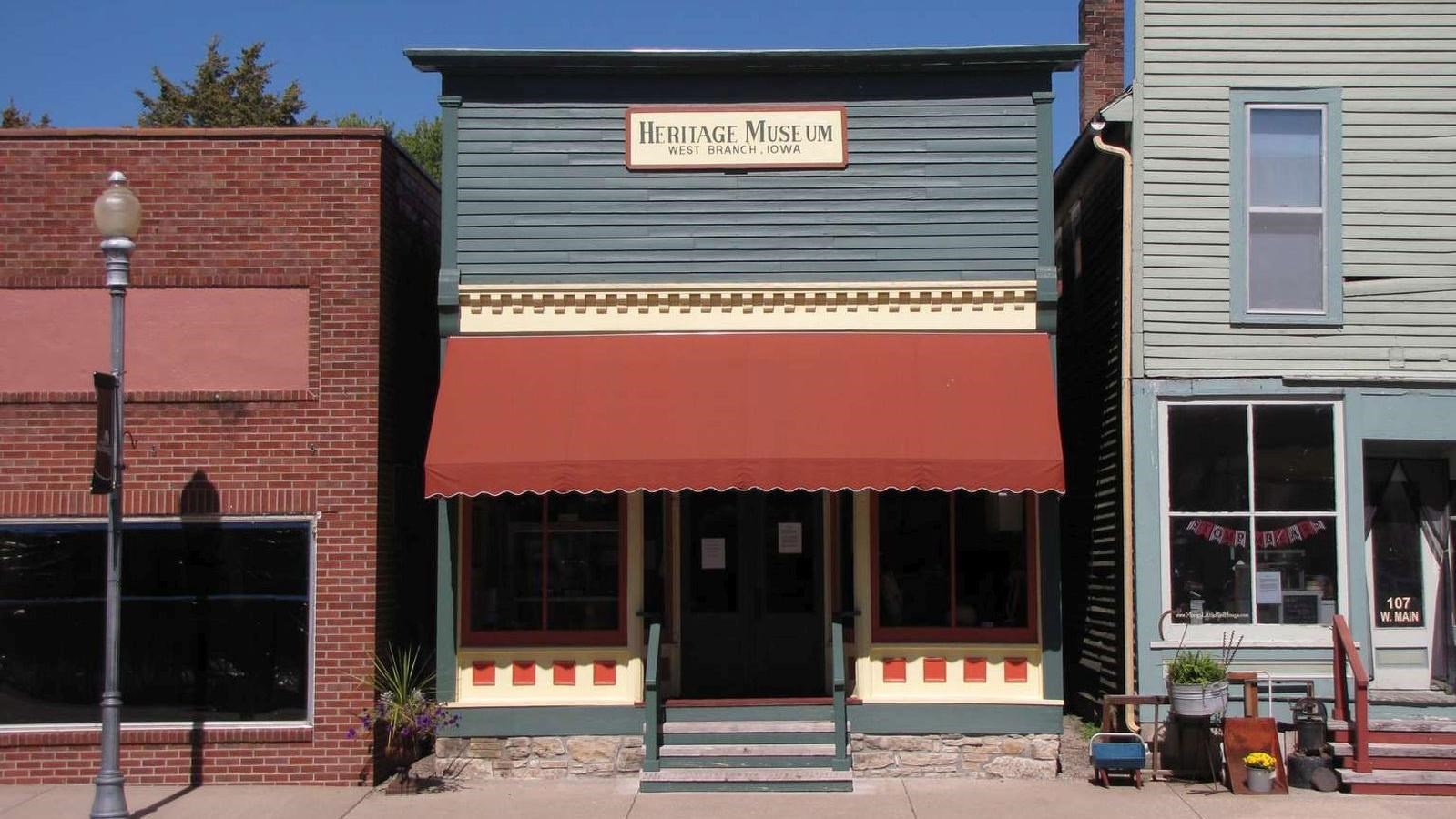 A wooden downtown building is painted dark green and has a red awning over the storefront.