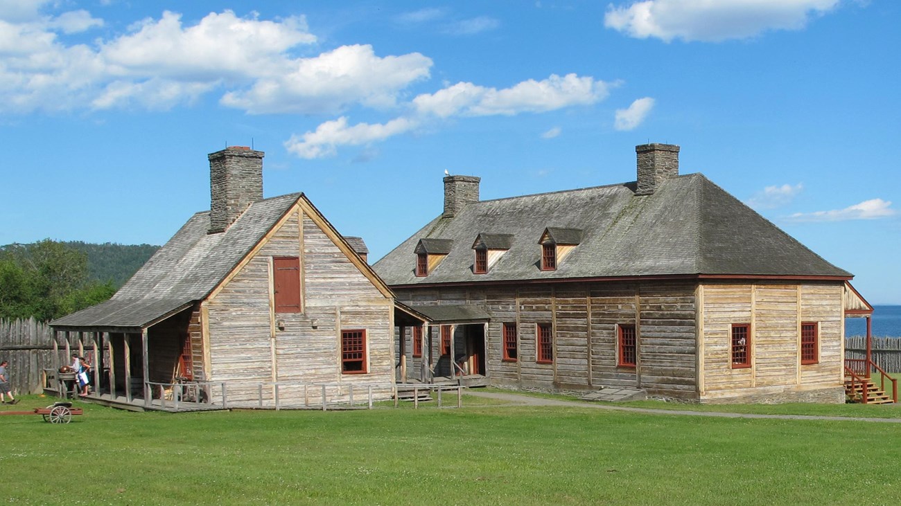 Reconstructed historic wood buildings on a lawn.