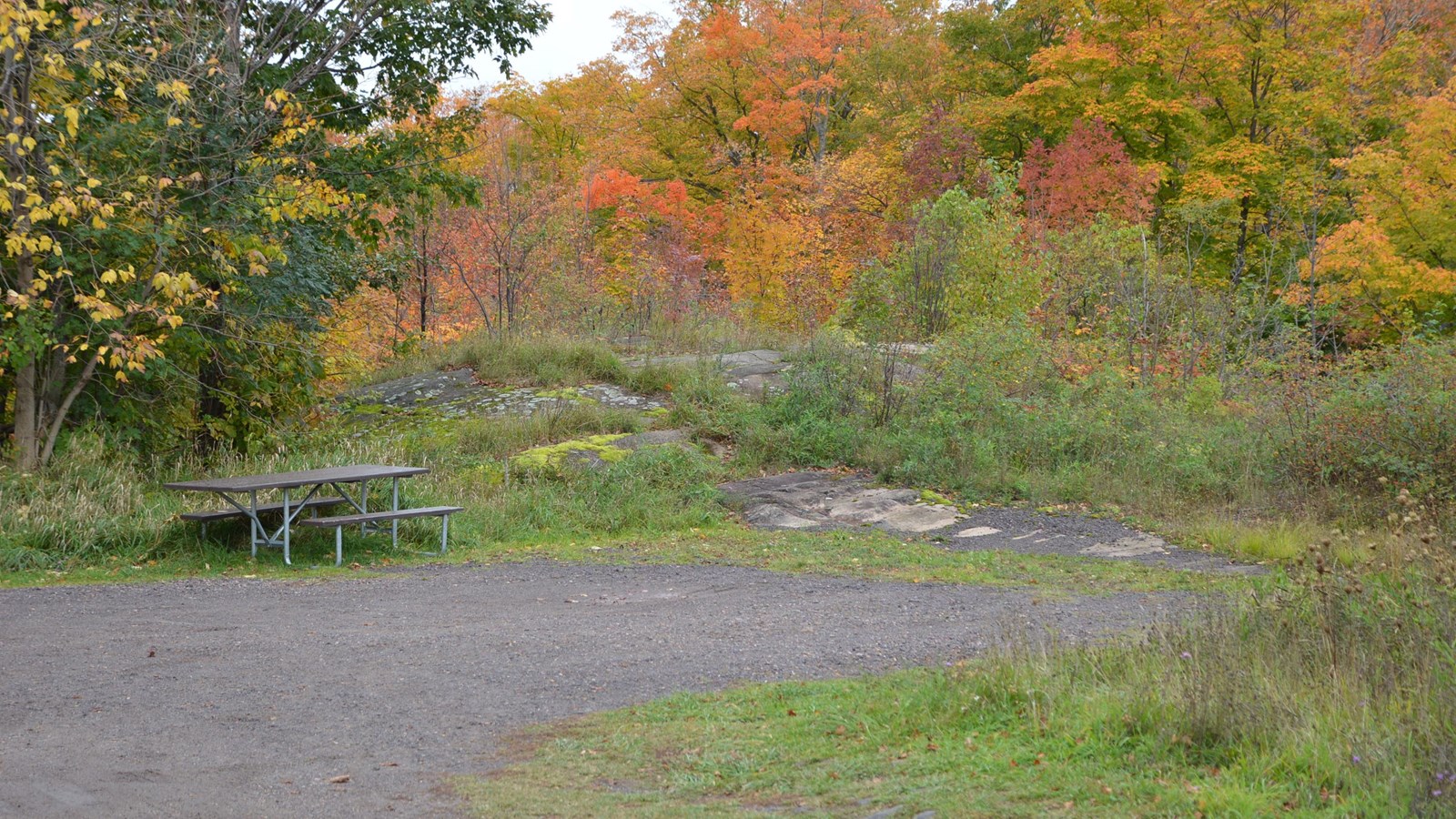 small parking area in wooded area with accessible picnic table and rock outcroppings 