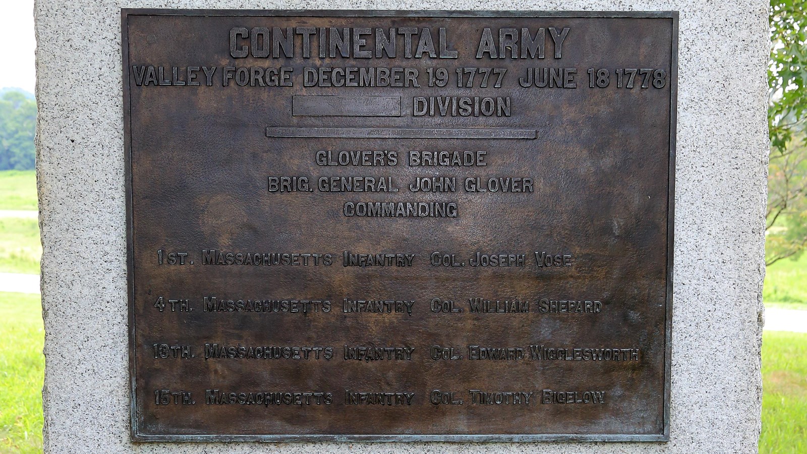 A large, smooth granite block with a bronze plaque, sides and bottom rough. 
