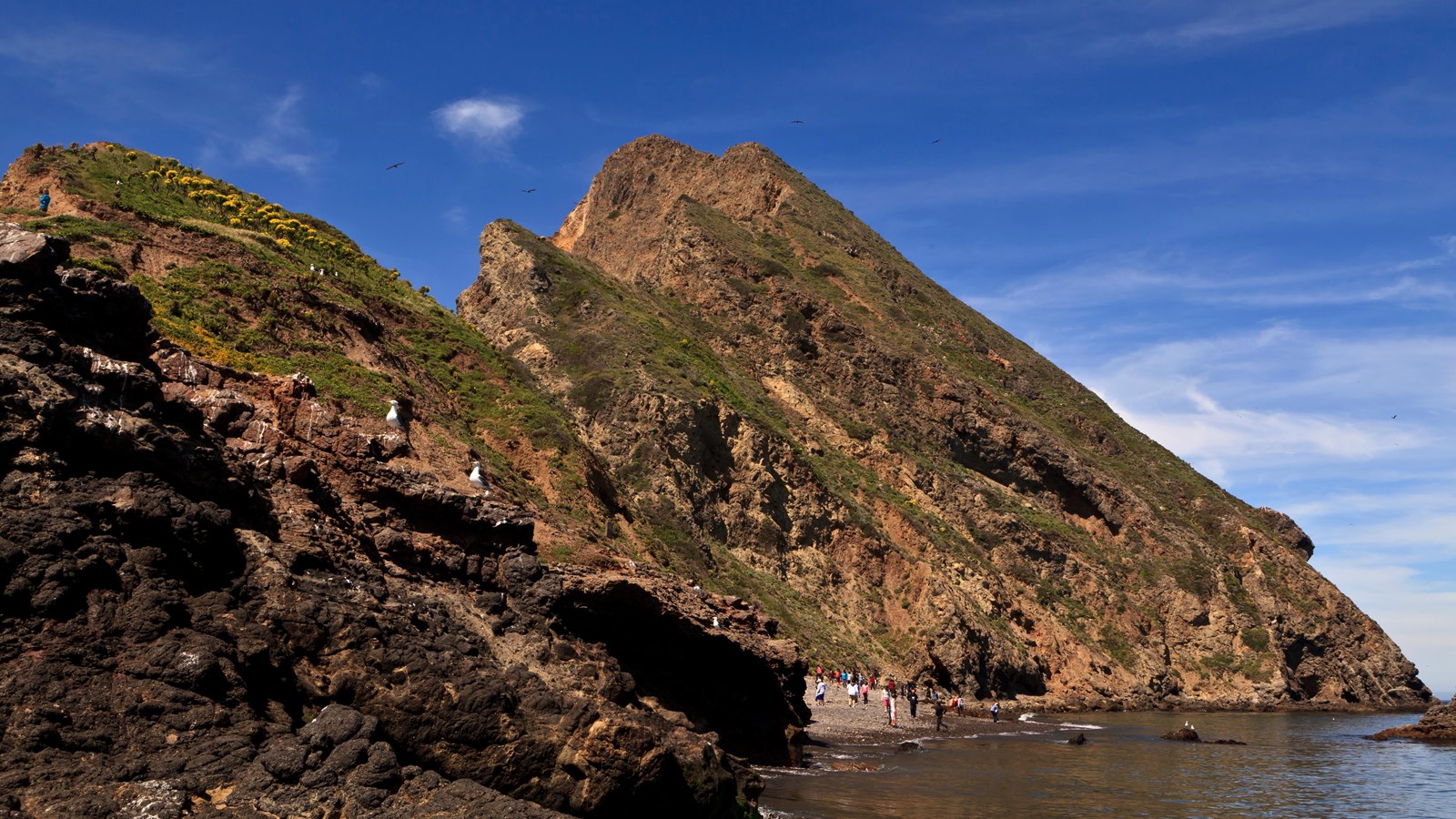steep rocky coast with small beach and visitors and boat offshore