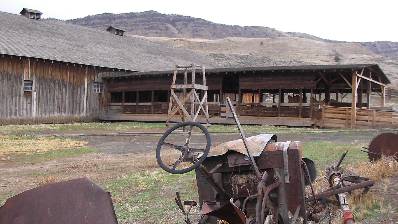 A corral with old farming equipment in the foreground.