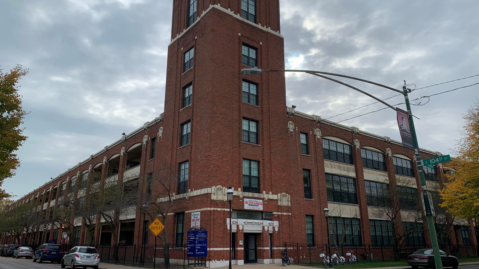 A three story brick building with a five story tower in the middle against a dark grey sky.