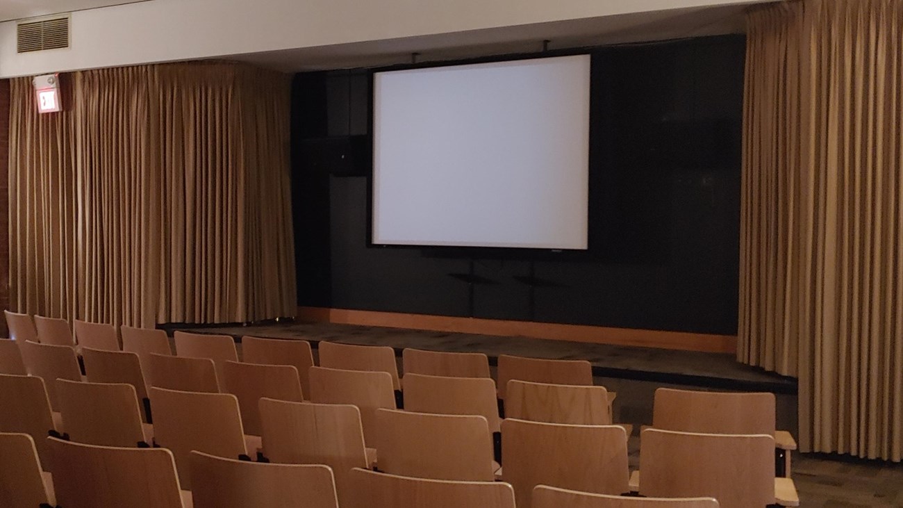 wooden chairs in row with a screen and a stage