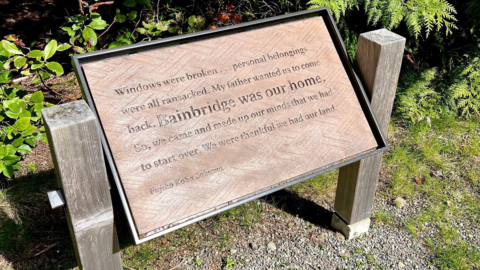 Brown plaque on gravel and vegetation.