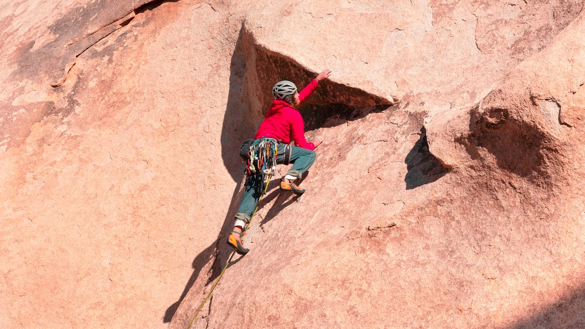 A rock climber making their way up a large reddish rock face.