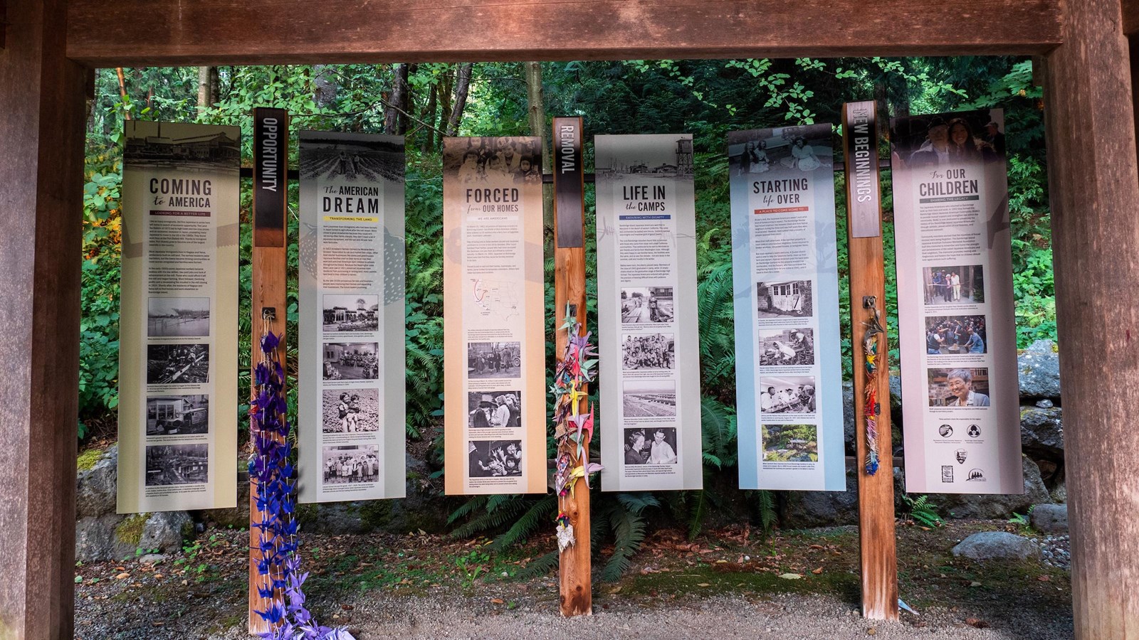 Six panels of text on a wooden frame against vegetation.