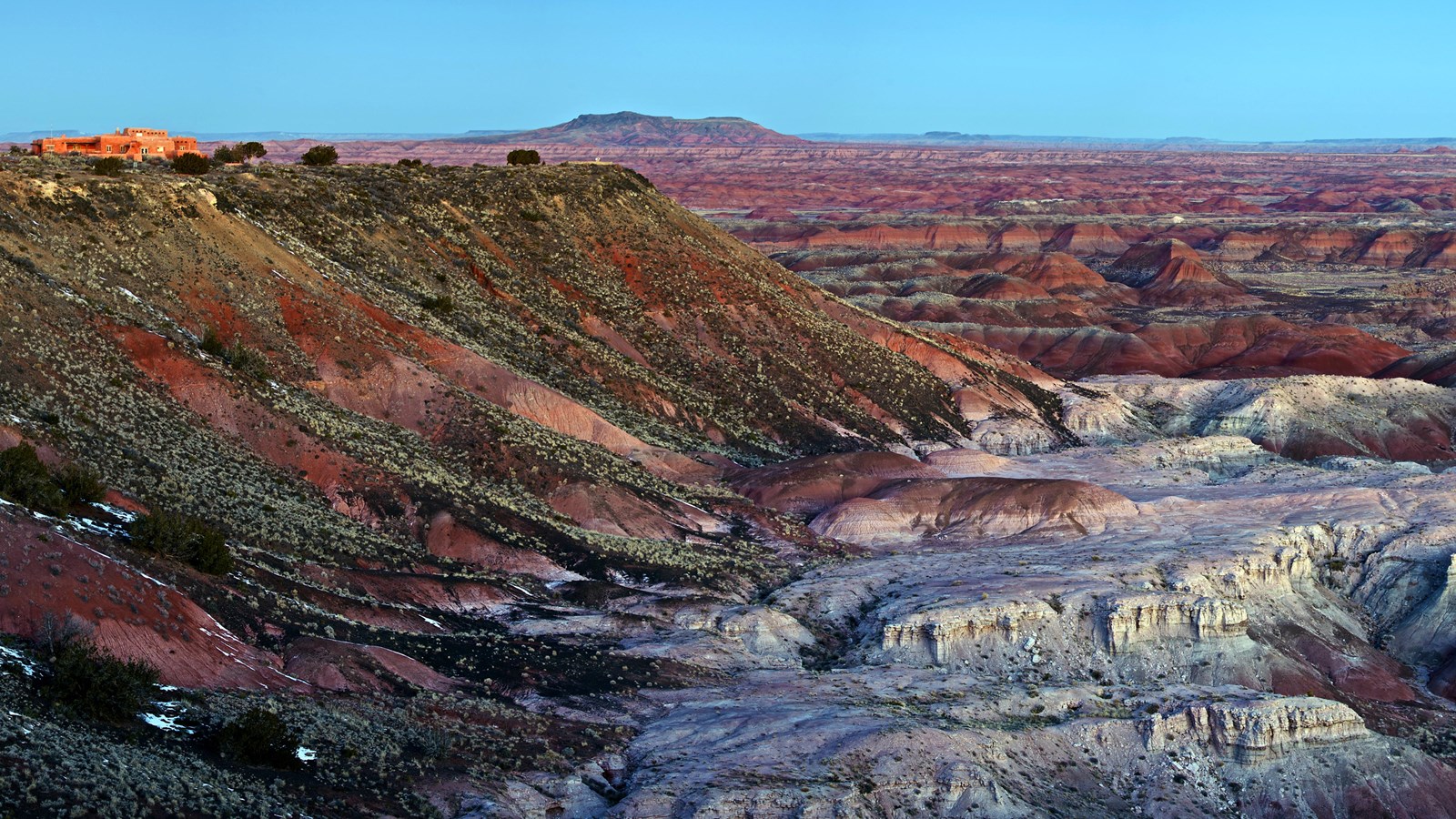 Overlooking white and red badlands from mesa edge at twilight, blue sky.