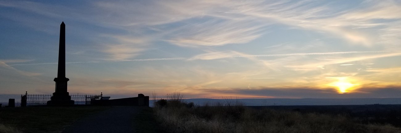 Silhouette of a monument and open field set against the sunset