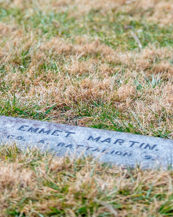 The dark colored gravestone engraved with the name Emmert Martin lays flat with the ground. 