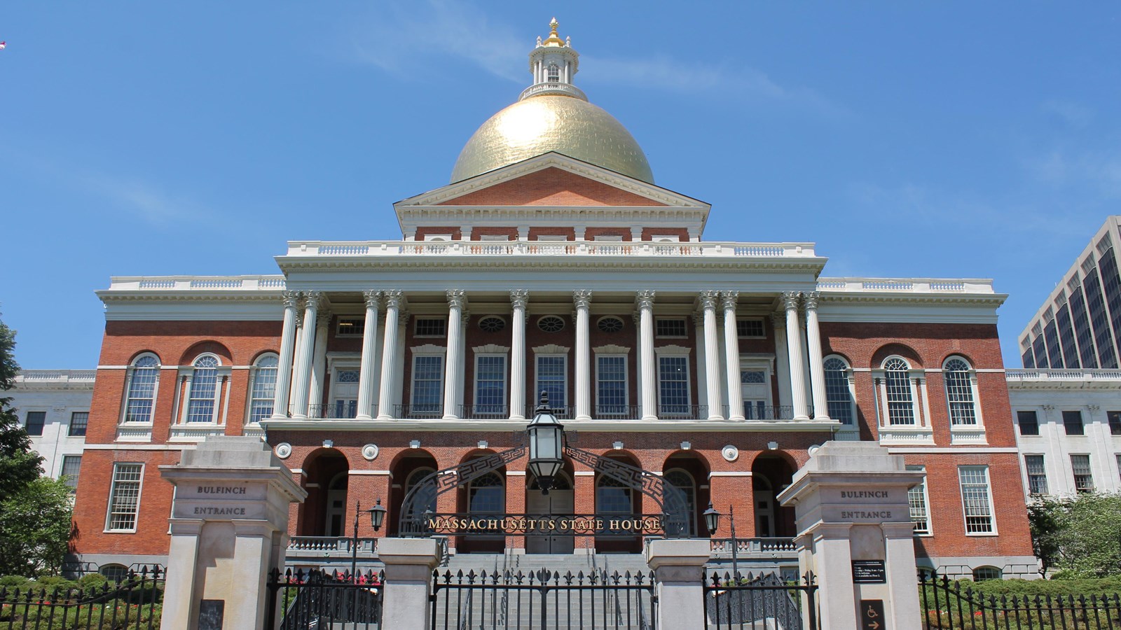 Red brick and white trimmed State House with a gold dome against a blue sky.