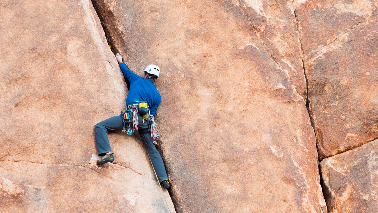 A rock climber making their way up a large reddish rock face.