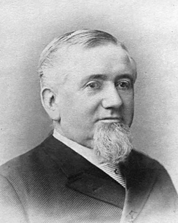 Black and white portrait of a man wearing a suit and tie with a white beard and hair. 