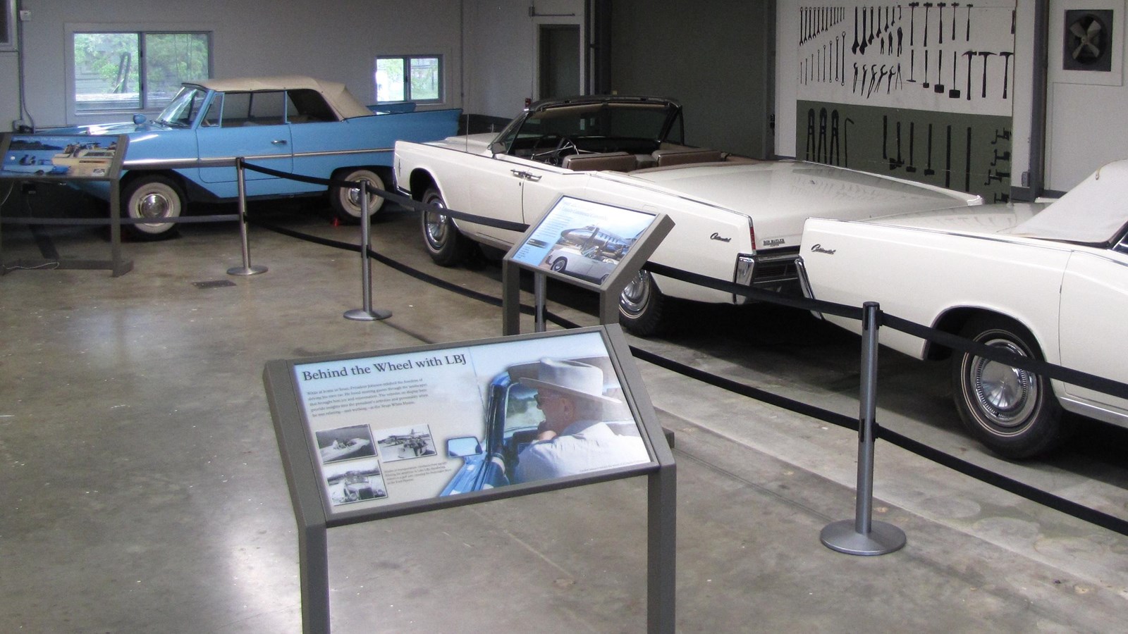 An exhibit sign stands in front of three historic car, all behind ribbon stanchions.