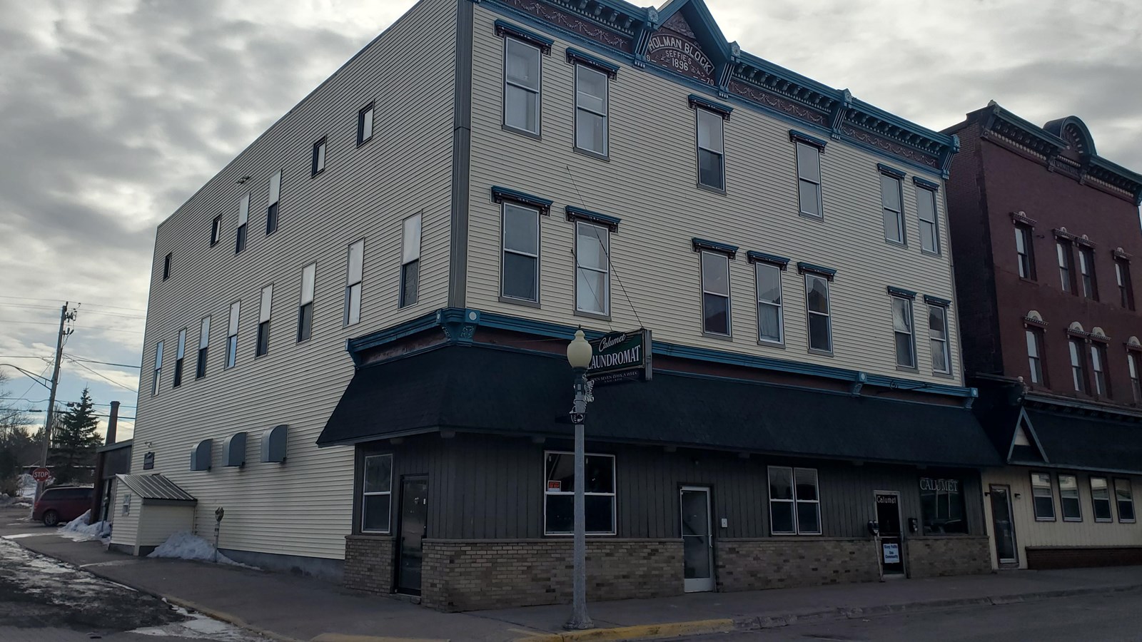Three story building with white siding. A sign at the top reads “Holman Block Seffie’s 1896.”