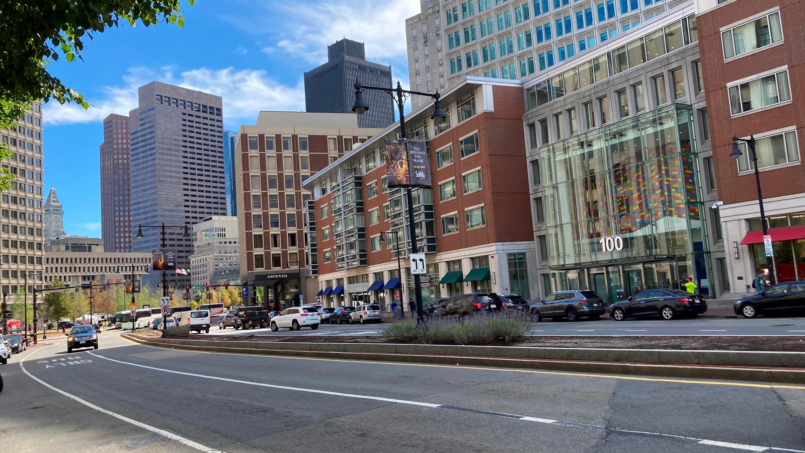 The curve of a four-lane city street separated by a planter divider. 5 story building lines street.