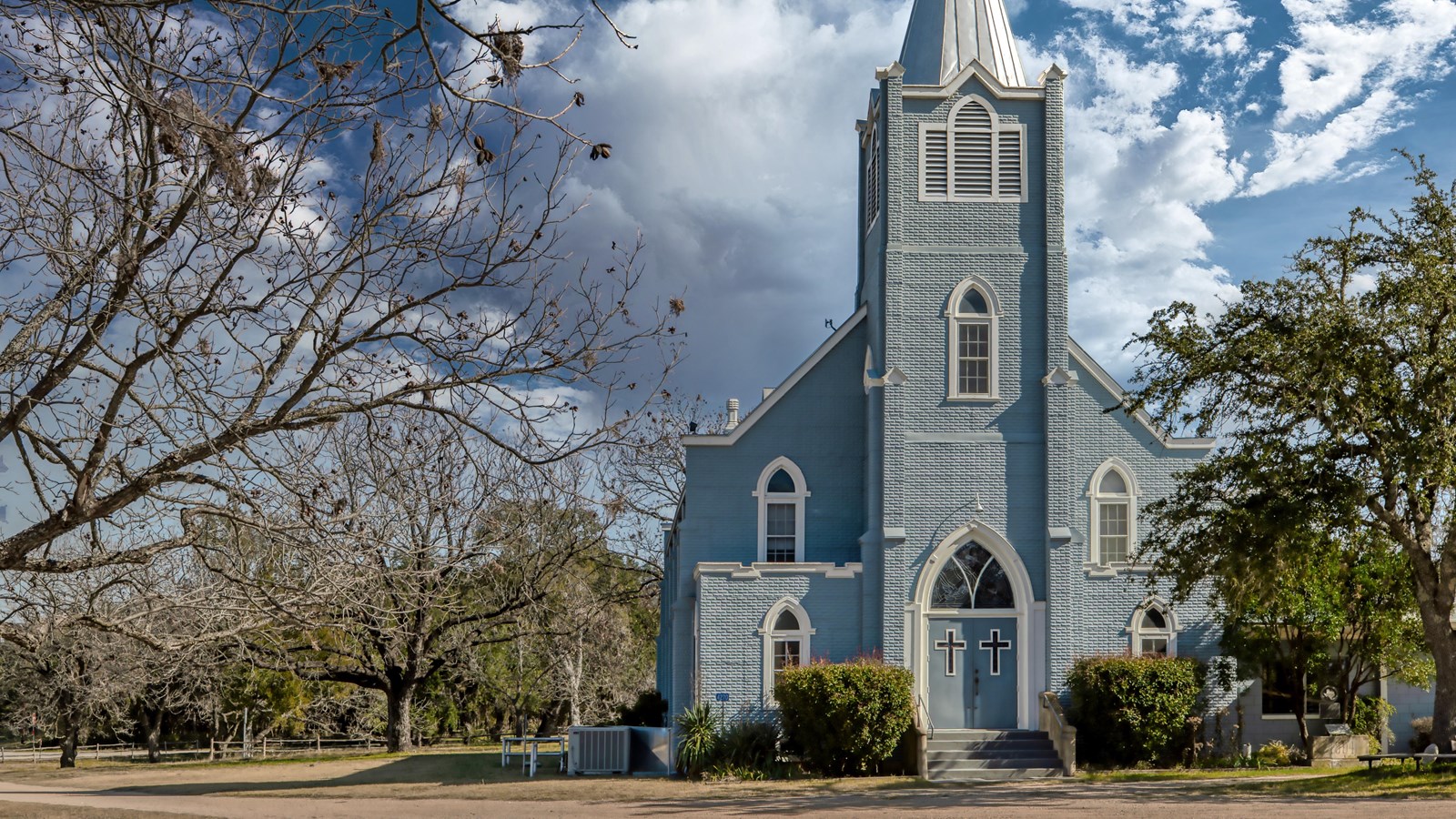 A gray-blue church with tall steeple stands against the backdrop of a bright blue sky.