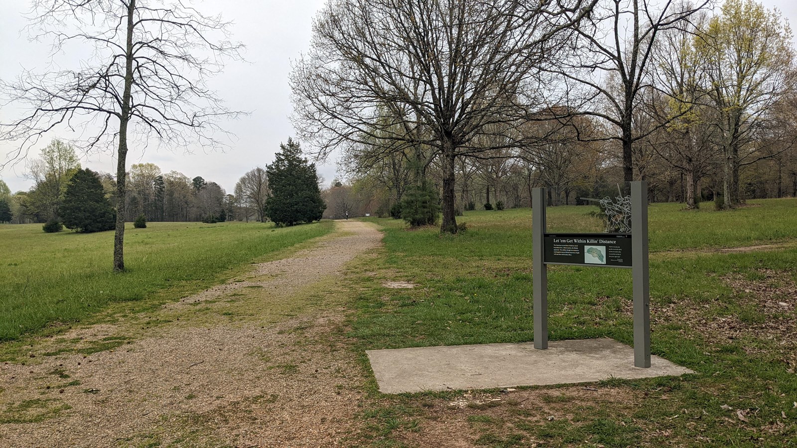 A way side next to a gravel road in a field with sparse trees.