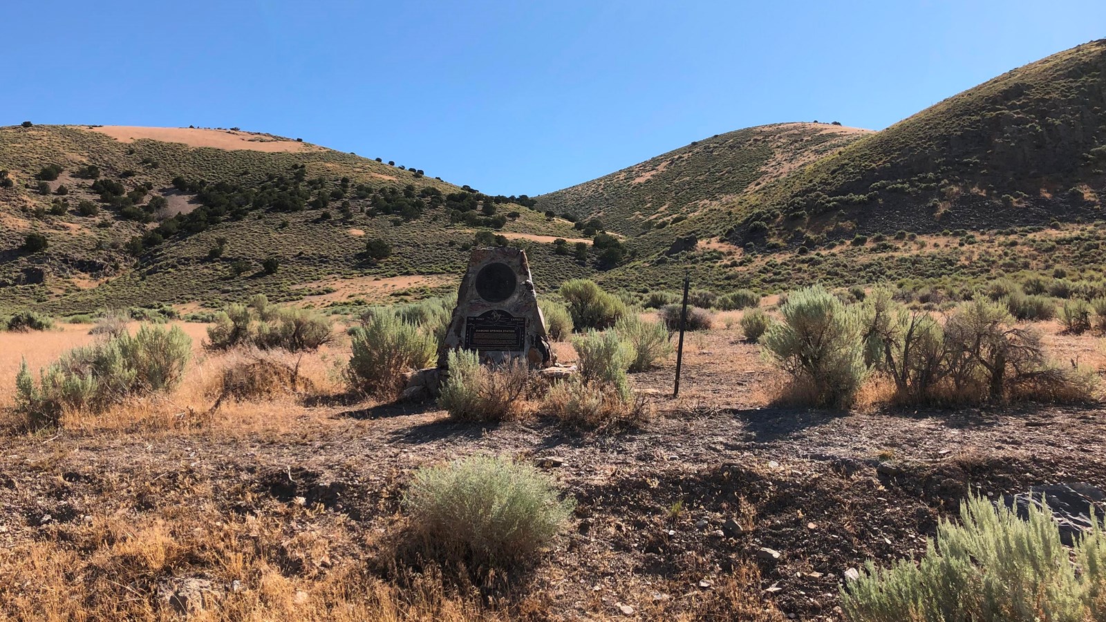 A squat stone and concrete monument stands at the foot of sagebrush-covered hills. 