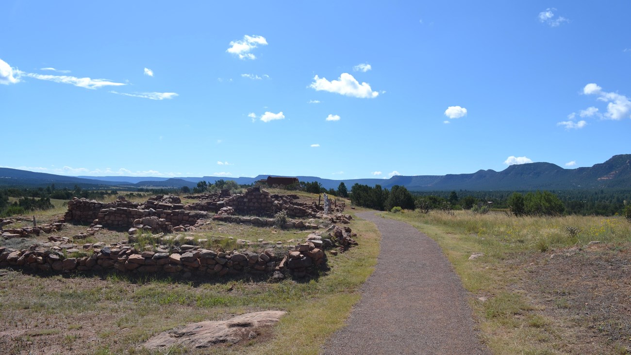 A trail passes by stone walls of the pueblo toward the adobe church.