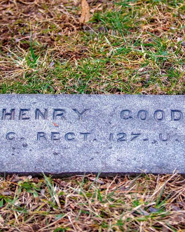 The dark gravestone engraved with the name of Henry Gooden lays flat with the surrounding grass.