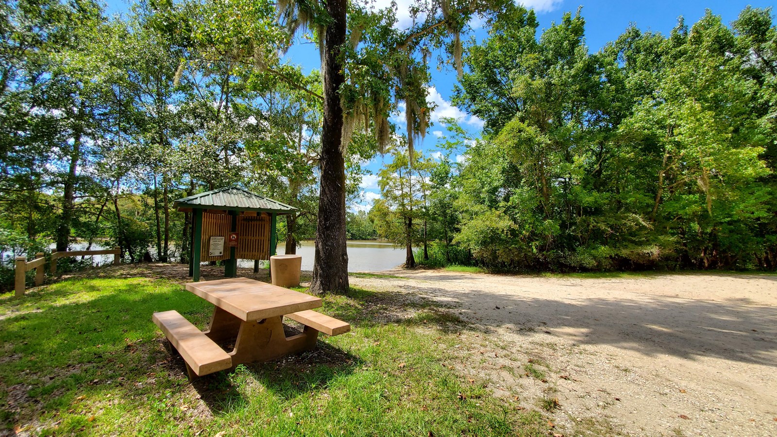 picnic table, trash can, and info kiosk next to dirt parking area and boat ramp