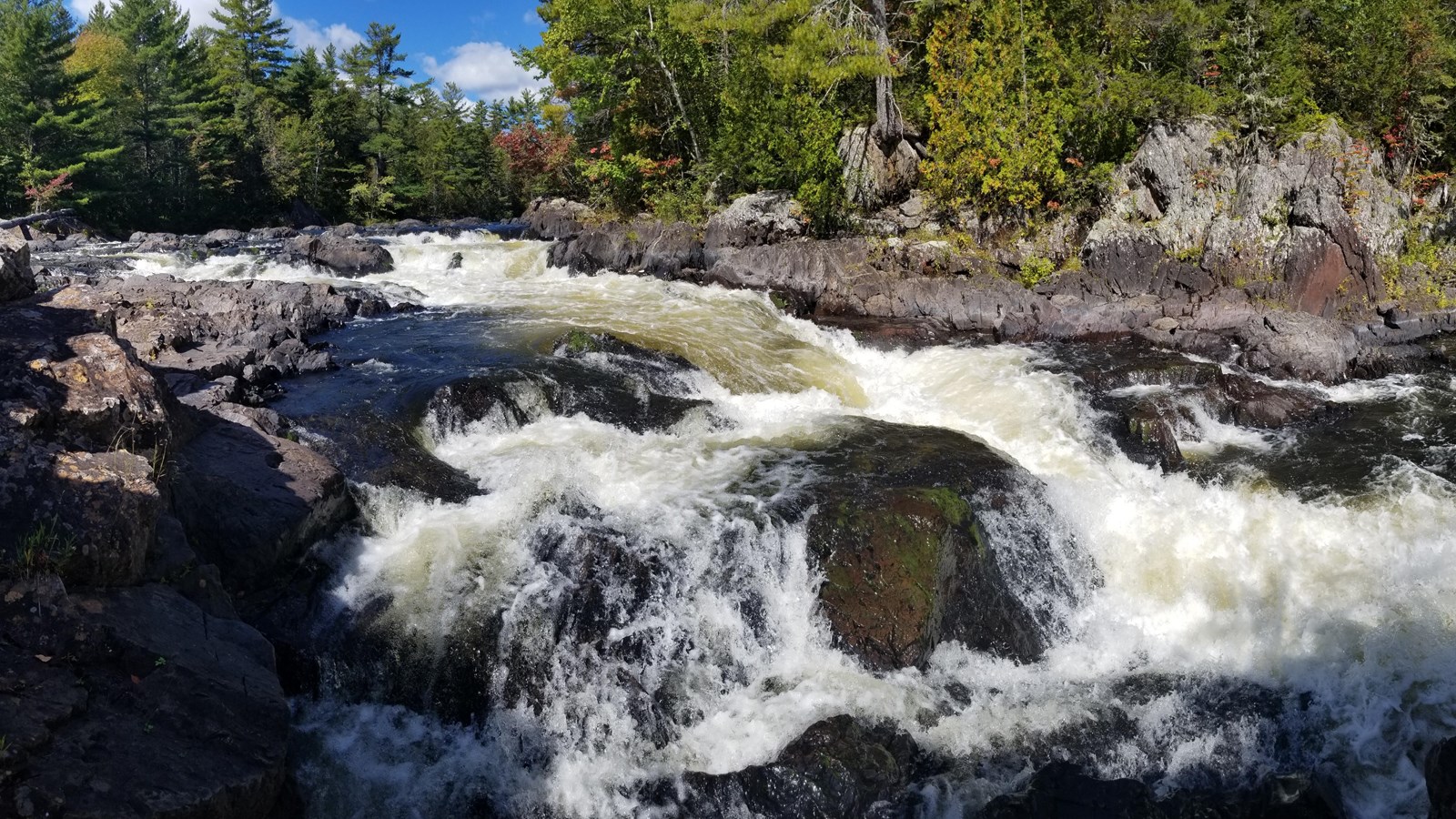 A large waterfall with granite cliff banks along the shores with forests above.
