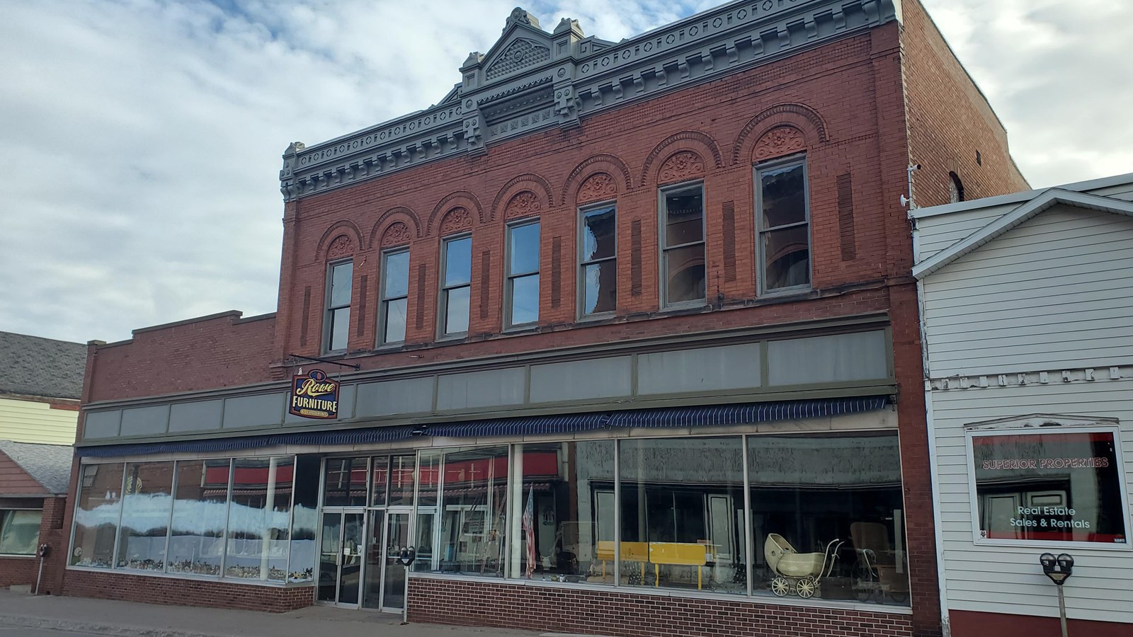 Two story brick building with large windows on the first floor and rectangular windows on the second