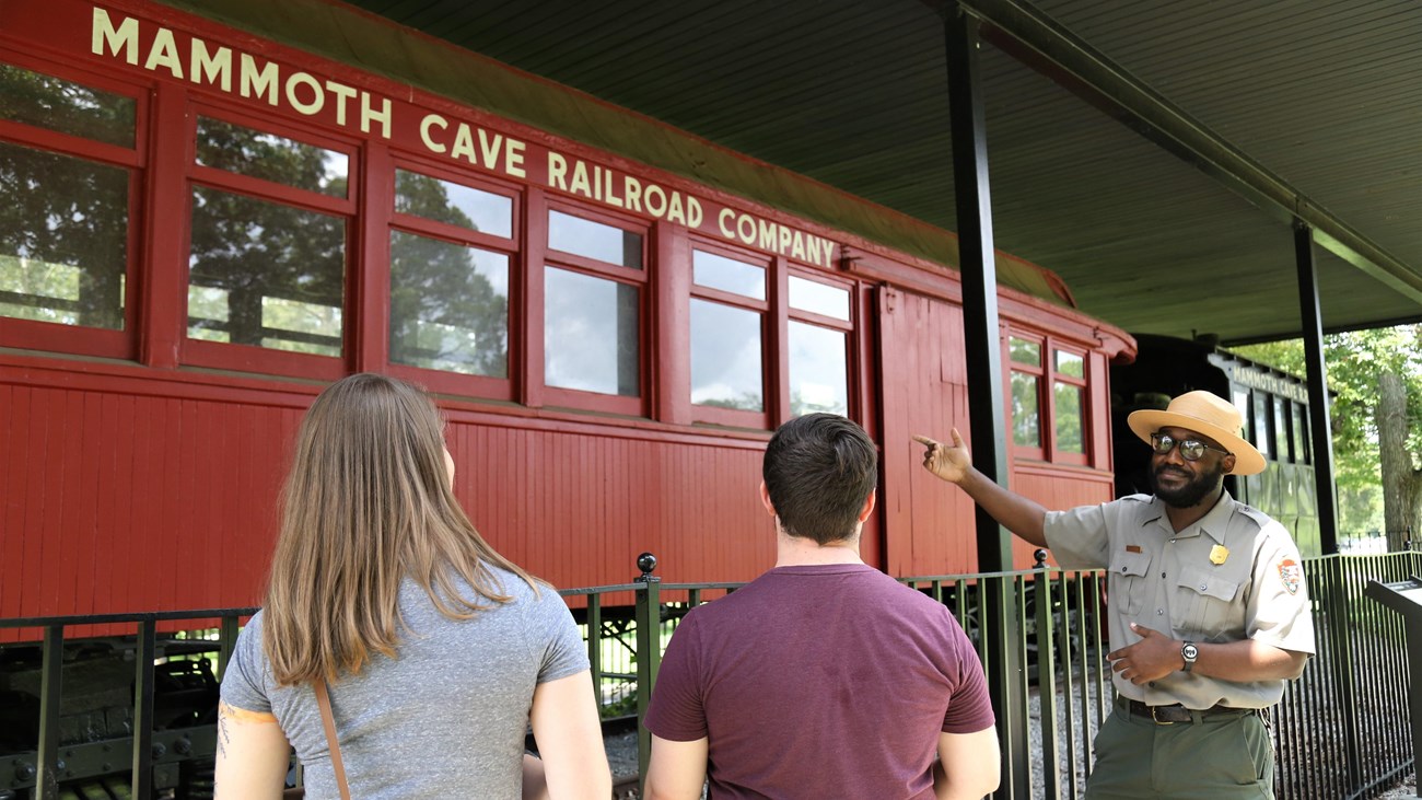 A ranger talks to two park visitors near a historic train