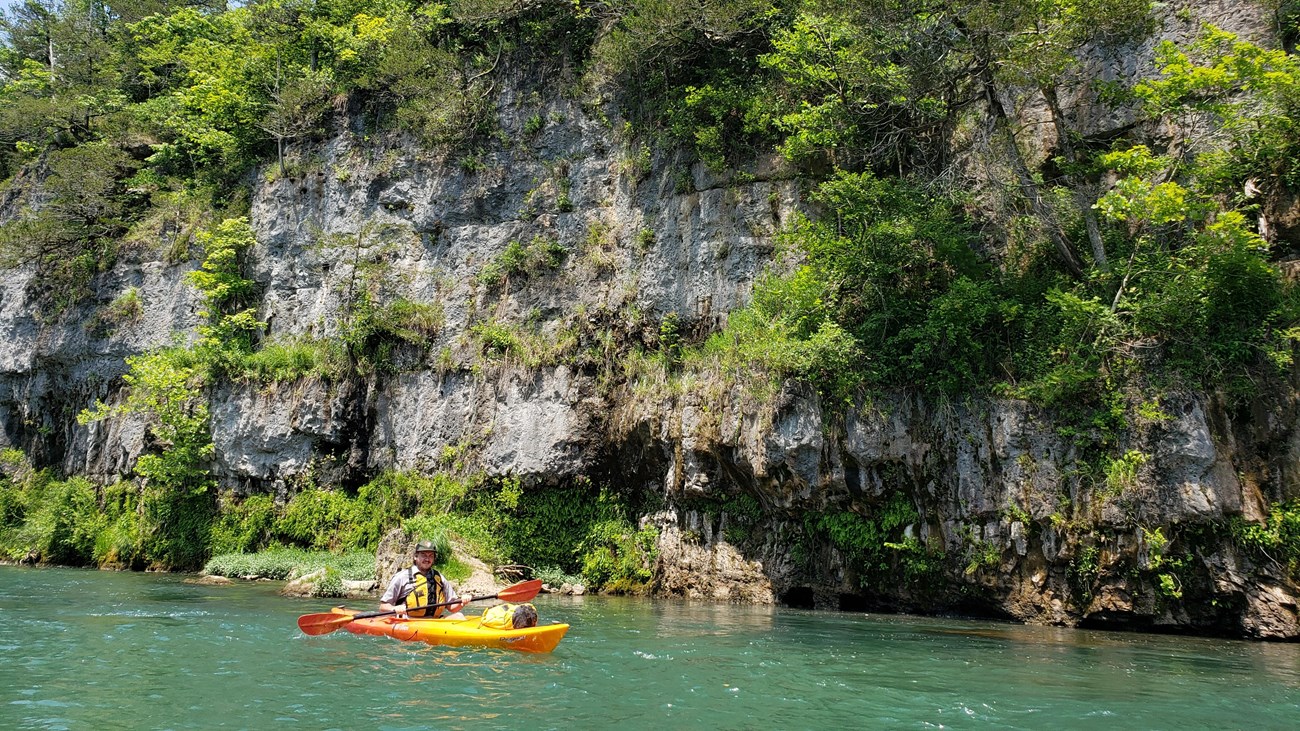 A yellow/orange canoe on a clear blue river with rock bluff in background