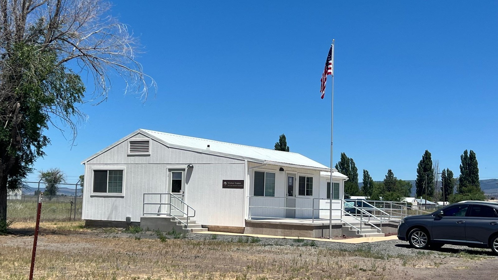 A white building with a US flag on a pole next to a car