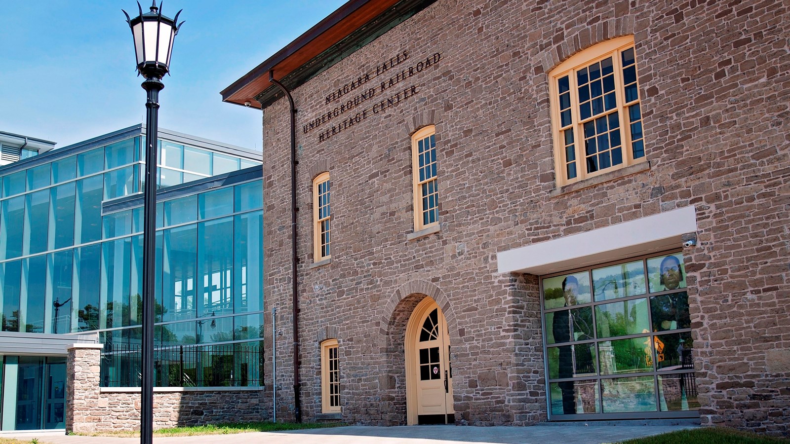 A brick building with four windows and a door. It is connected to two smaller glass buildings.