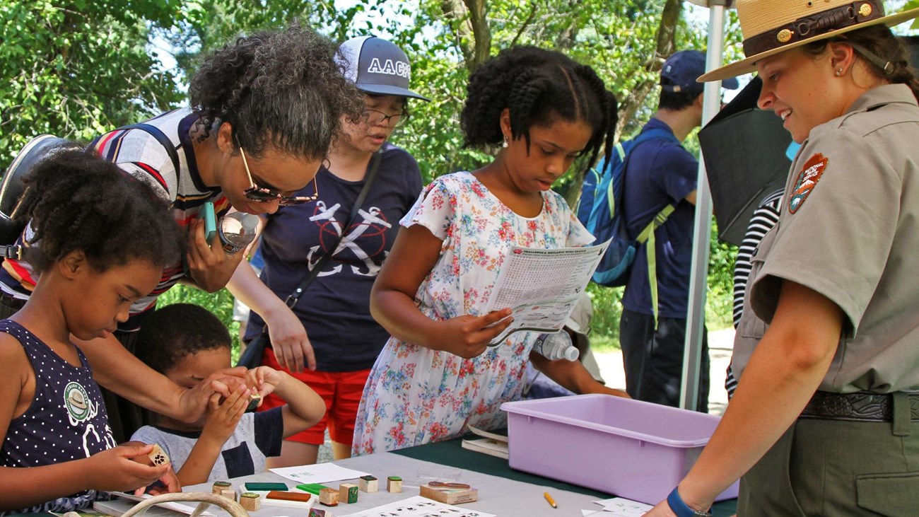 a group of kids with a park ranger looking at antlers on a table.