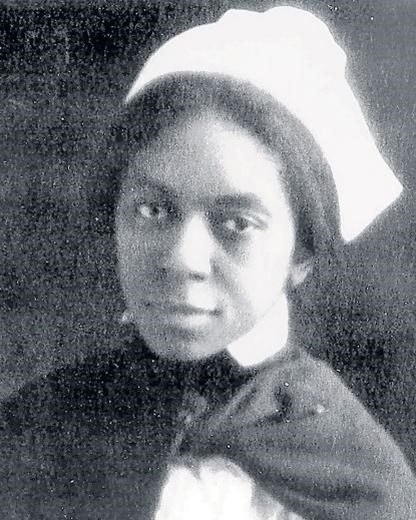 Black and white photo of African American women in WW1 nurse uniform standing with arms crossed.