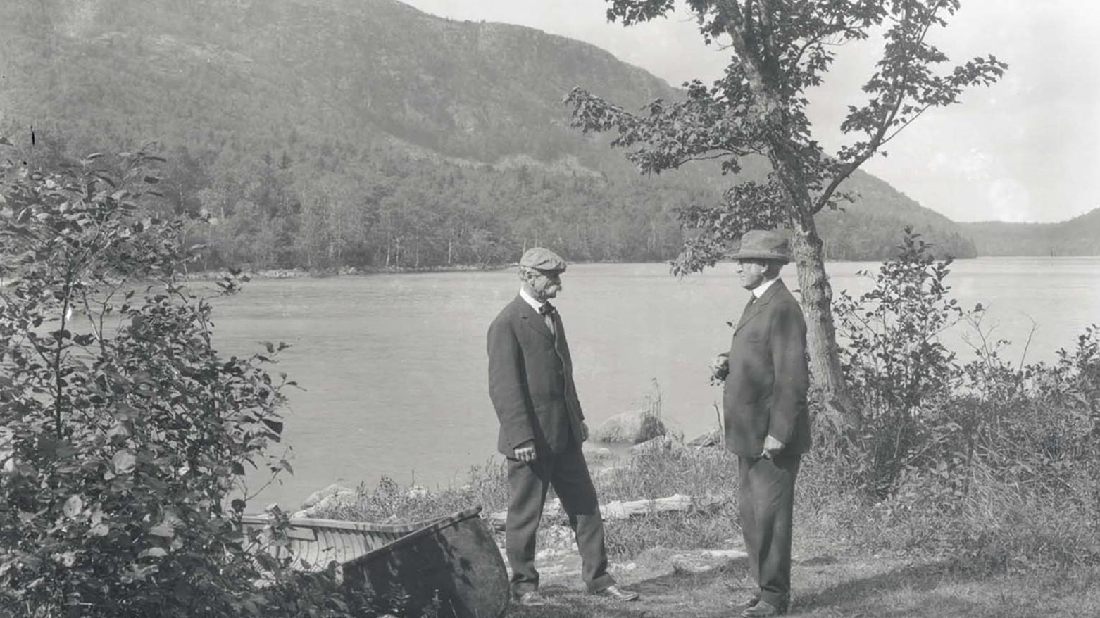Two men stand in front of a lake.