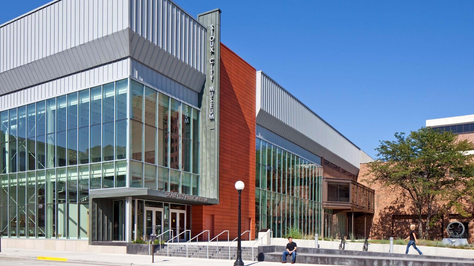 A rectangular, multi-level building made mostly of glass, with one section made of red terra cotta.