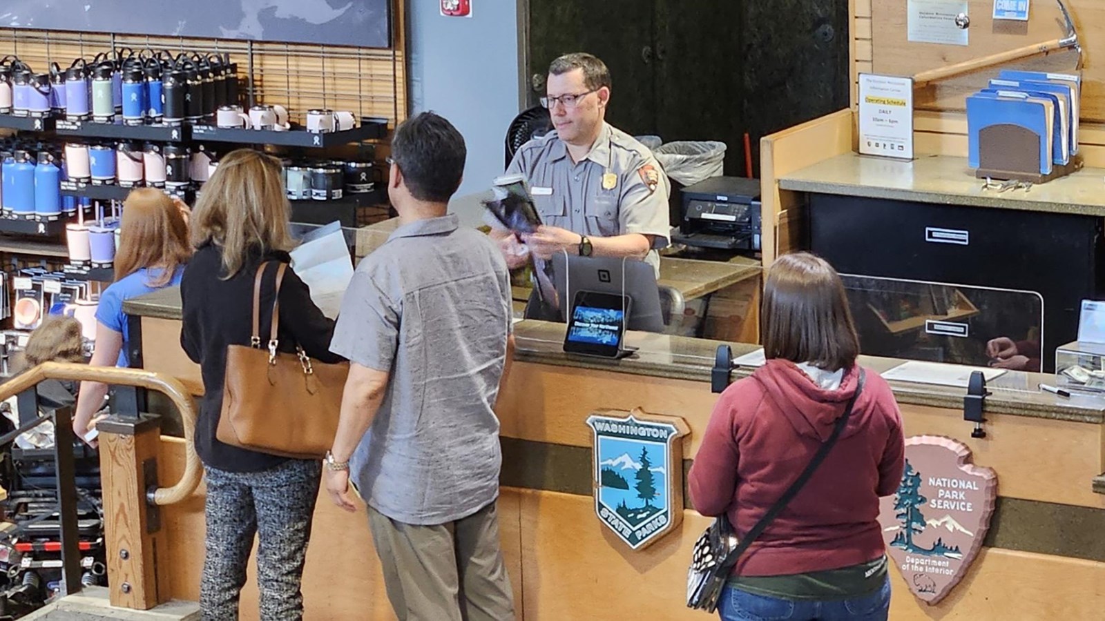 Uniformed ranger behind a wooden desk helping a variety of people.