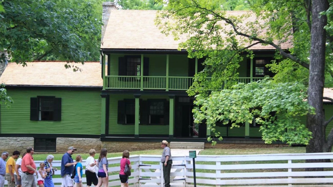 Park Ranger leading a large group of people towards the front gate of a green two-story house.