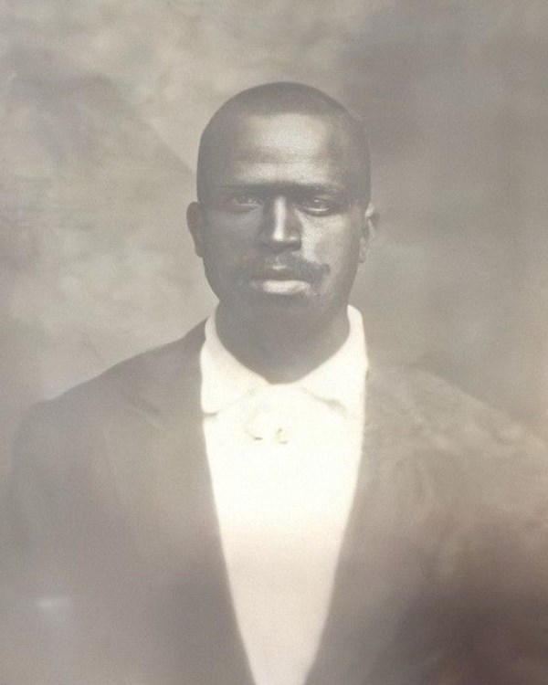 bland and white portrait of black man in white button down shirt and black suit coat