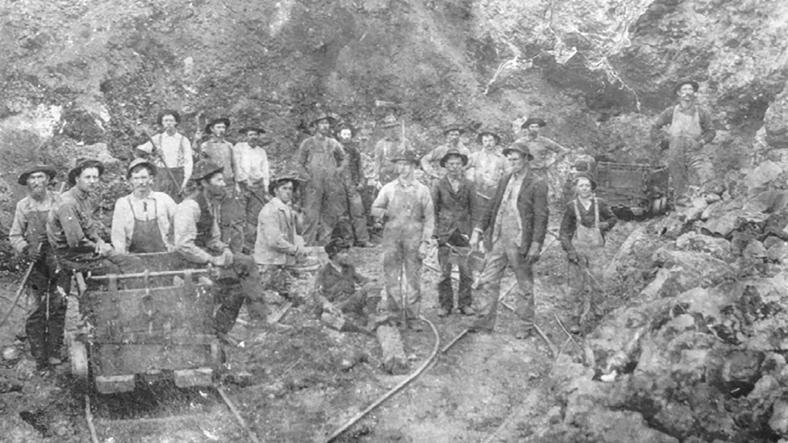 A black and whit photo of 27 workers with a mine cart on rails