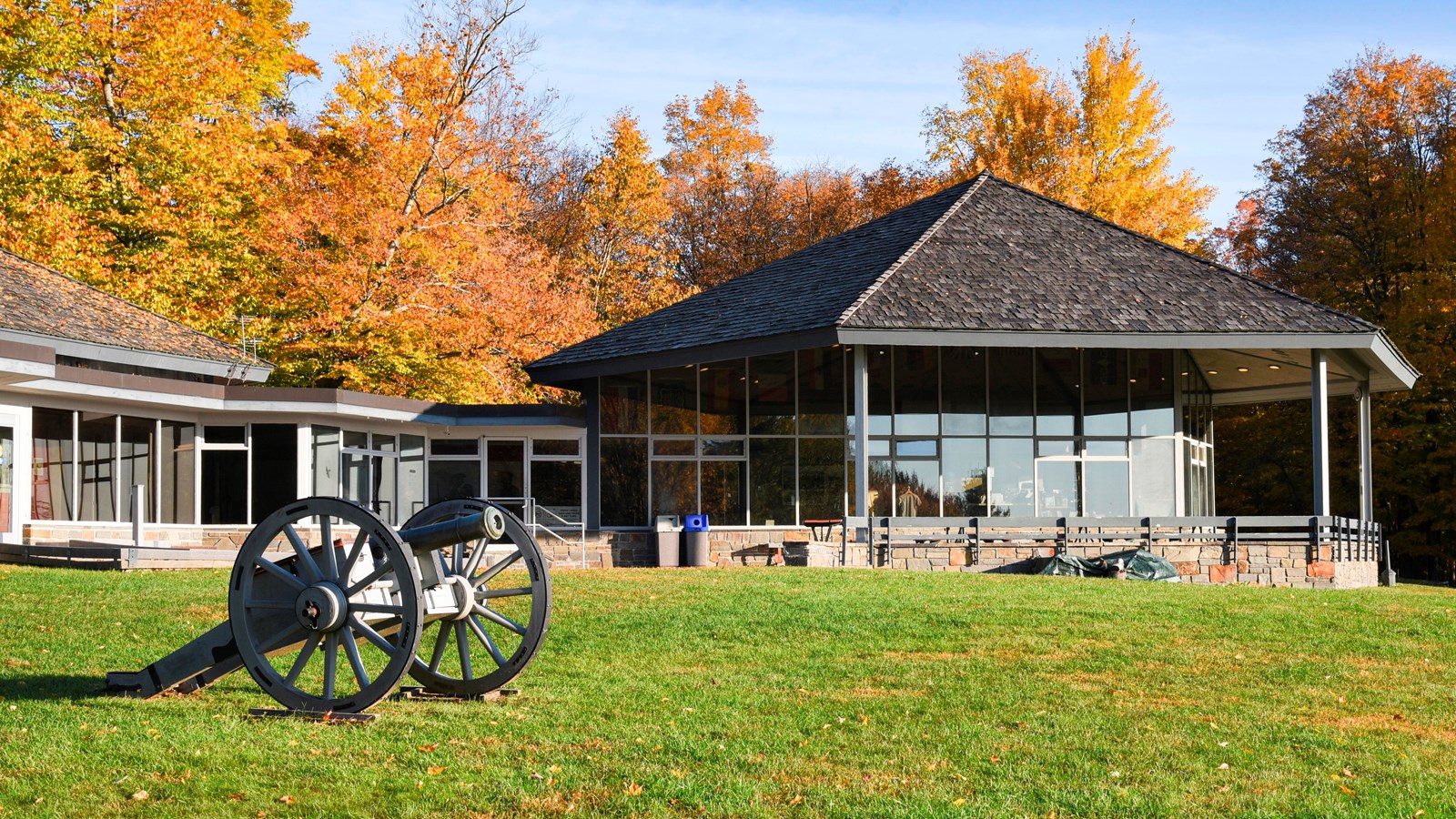 A small canon sits on a grassy lawn in front of a window covered building