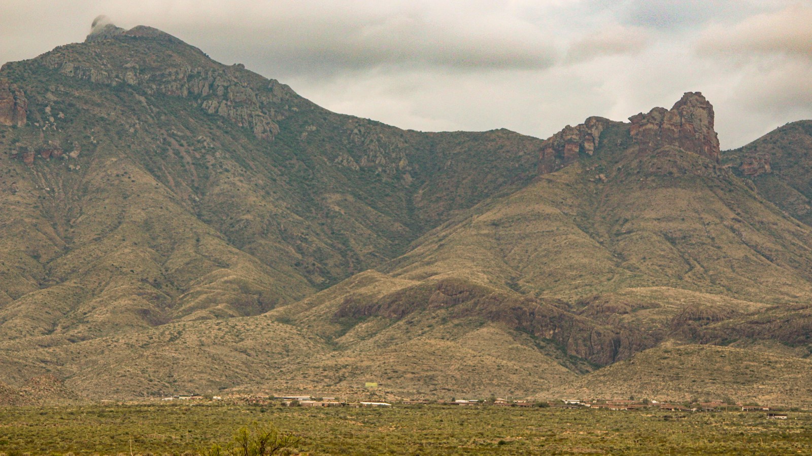 Around 60 buildings dot the landscape below two large peaks in a mountain range.