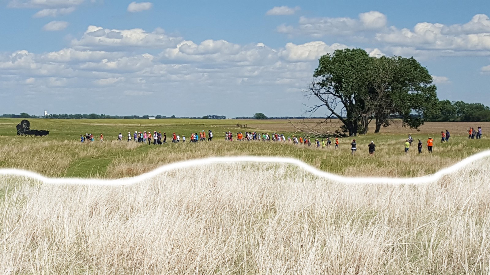 Flat, open field of grass, with two areas where there is an eroded swale. People walk across it.