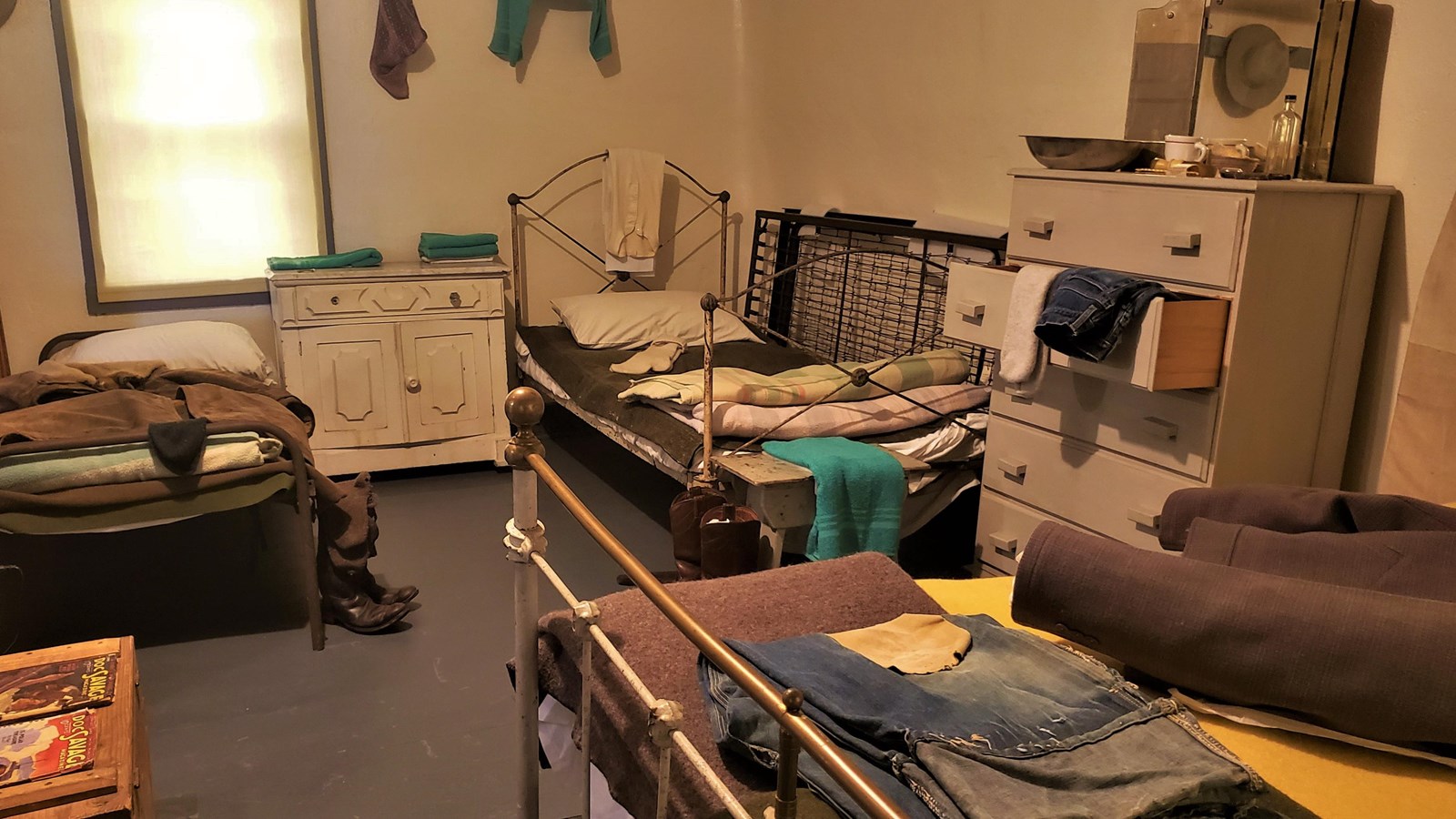 A small sleeping space for cowboys that contains three beds and scattered personal items.