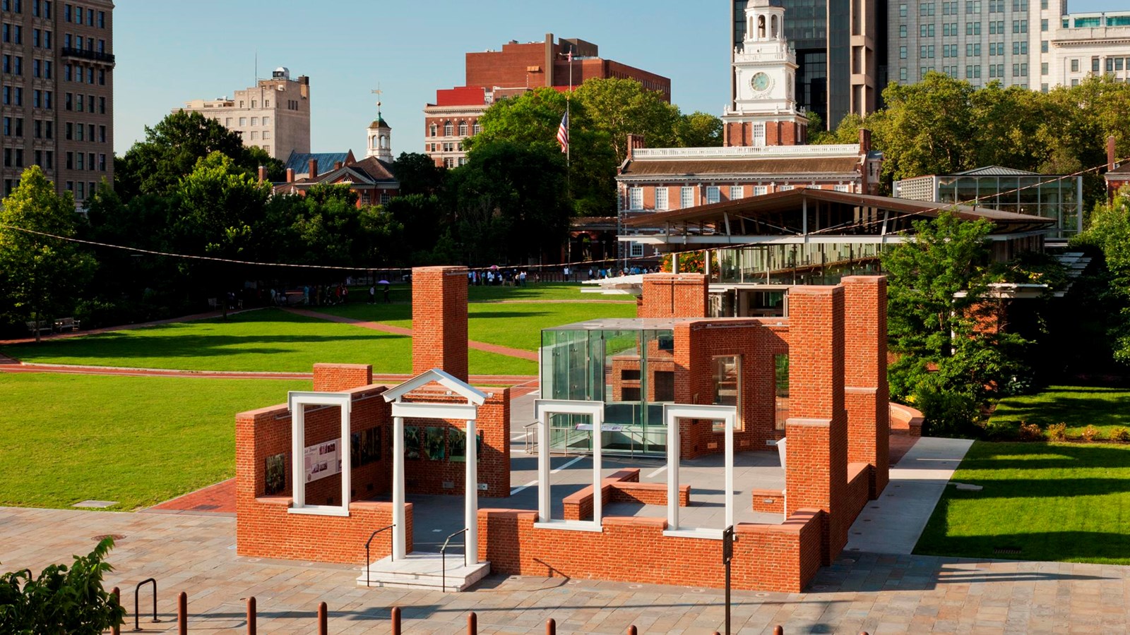 A color photo showing the President\'s House site exhibit with Independence Hall in the background